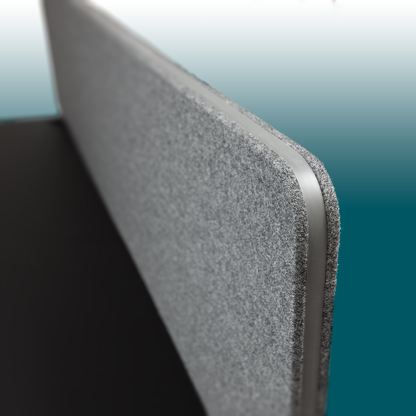 Close-up view of the top edge of a dark grey EDGE acoustic desk partition. Felt surface with a fine texture, edged with a rounded dark grey rubber trim. Background: a gradient from light blue to turquoise.