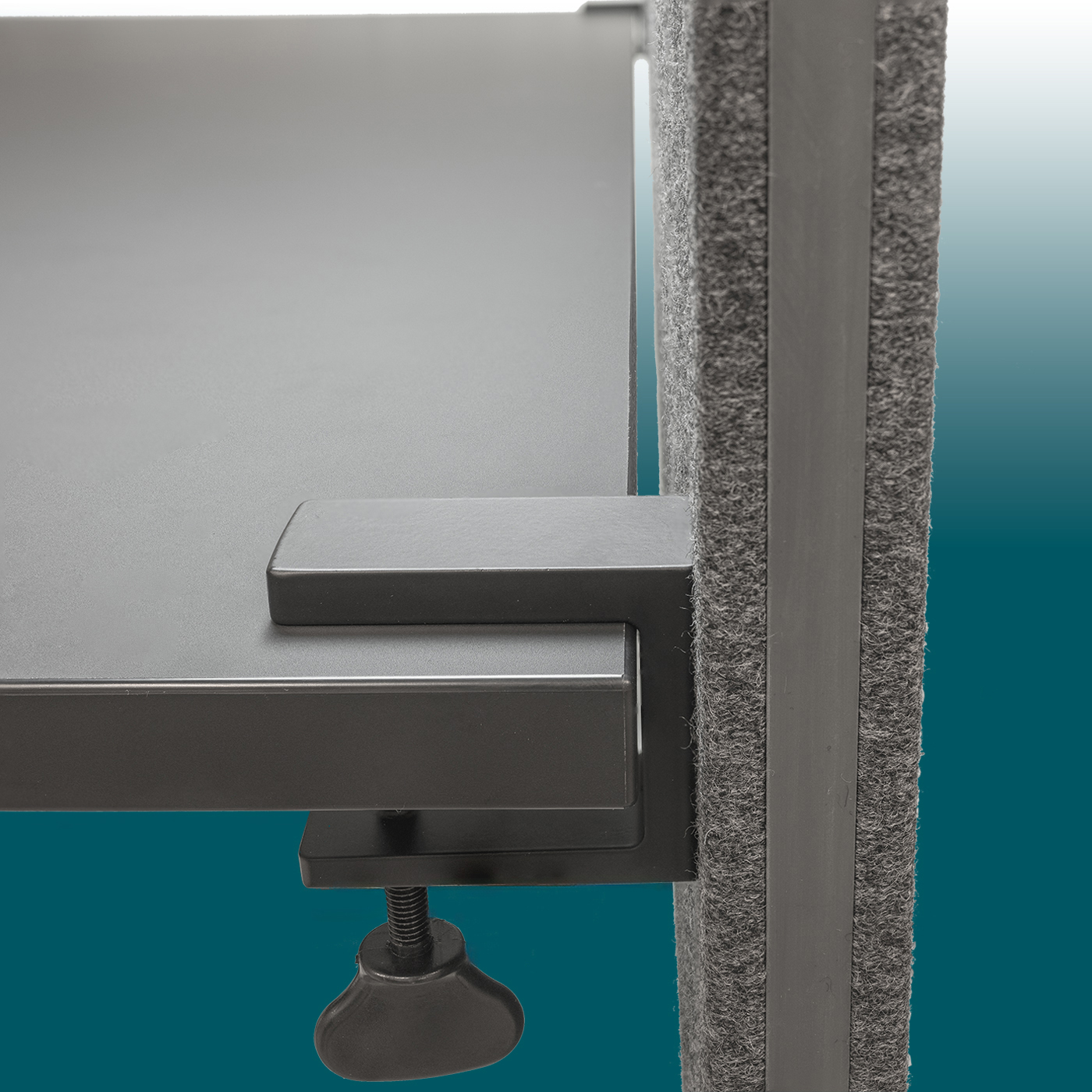 Detailed view of a dark grey, felt-covered acoustic desk back panel attached to a desk top. A dark grey metal clip with a black rotary knob secures the partition. Vertical side with a rubber edge and felt texture.